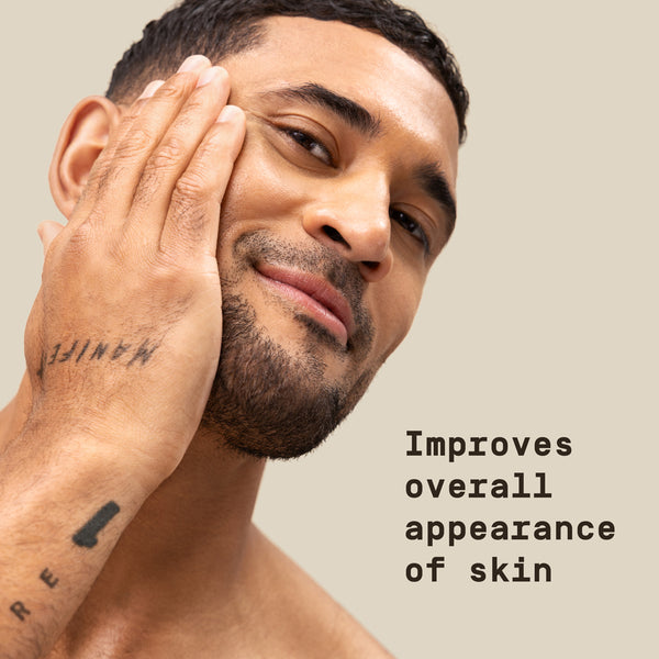 Man with a tattoo on his arm touching his face against a beige background with "improves overall appearance of skin" text overlay.