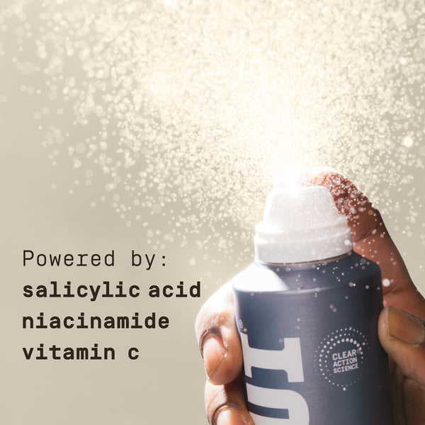 Hand holding a clear action science PAPATUI Acne Fighting Body Spray product with text about ingredients on a light background with salicylic acid, niacinamide, and vitamin c.