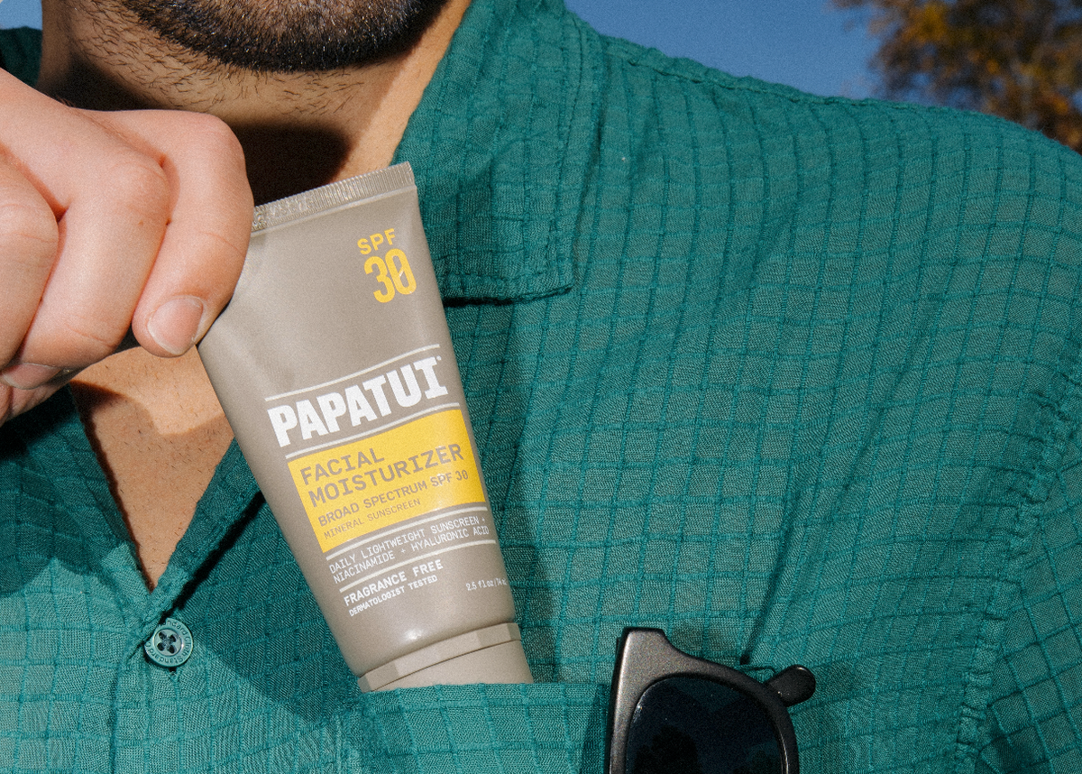 Close-up of PAPATUI Facial Moisturizer with SPF in man's shirt pocket against a nature background