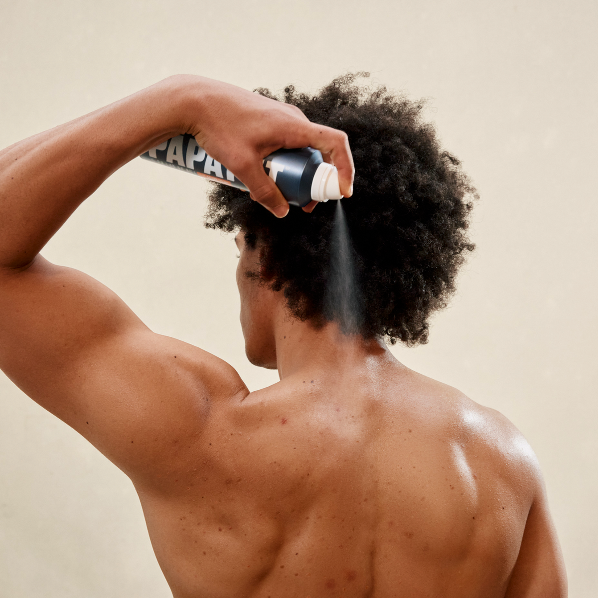 Man spraying PAPATUI Acne Fighting Body Spray on his back against a neutral background