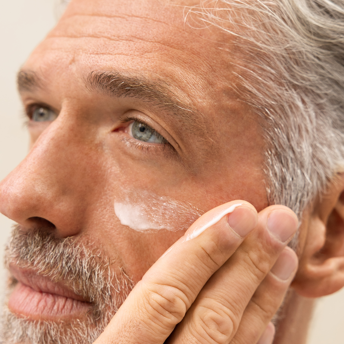 Close-up of man applying white cream to his face against a neutral background