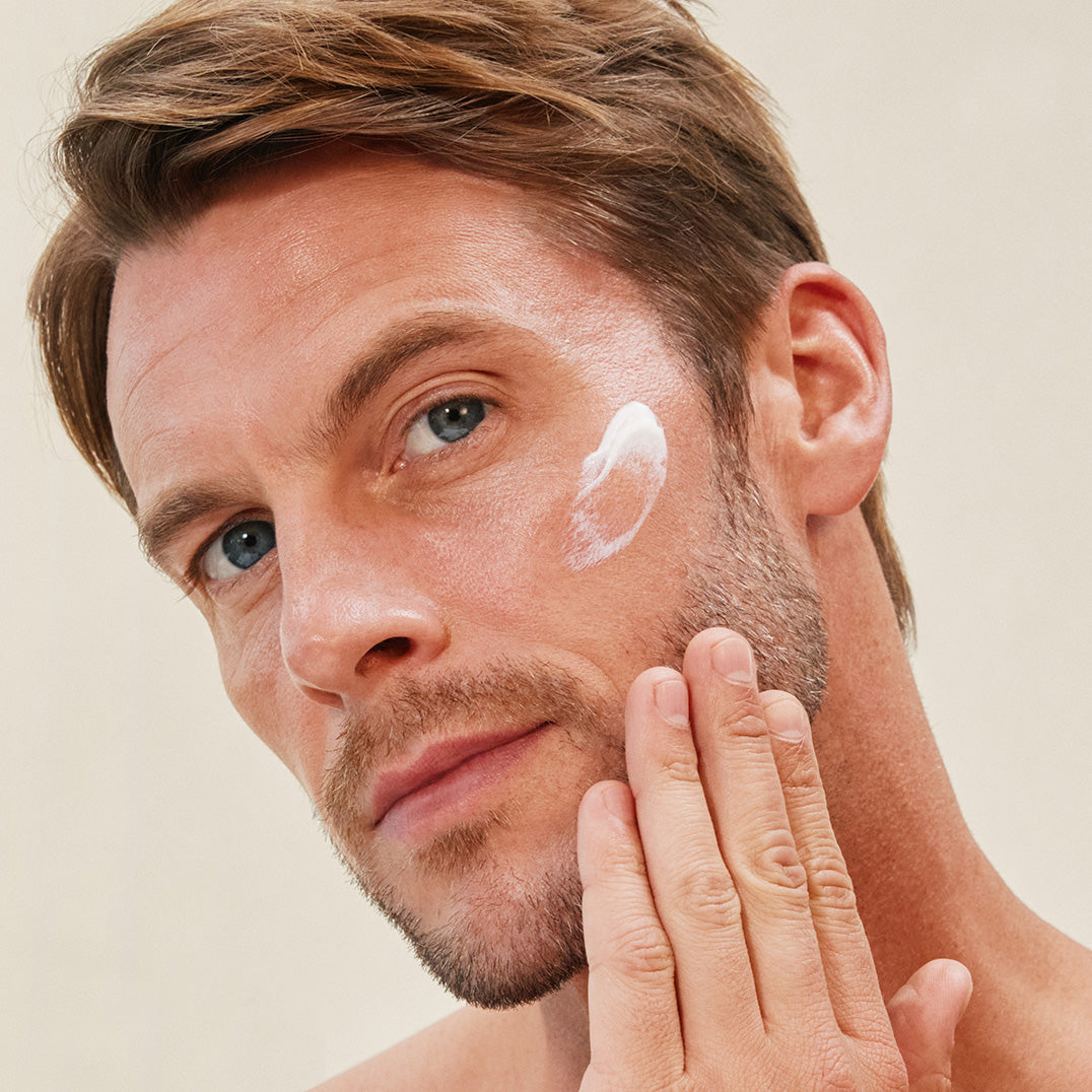 Man applying white cream to his face against a neutral background
