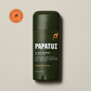 A dark brown stick of PAPATUI 48-Hour Antiperspirant Deodorant in Sandalwood Suede scent, positioned on a beige background with small dark twigs to the side. The product features orange and white text on the label, promising 48-hour sweat and odor protection, invisibility on clothes, and long-lasting freshness. The deodorant's size is indicated as 2.6 ounces or 73 grams.