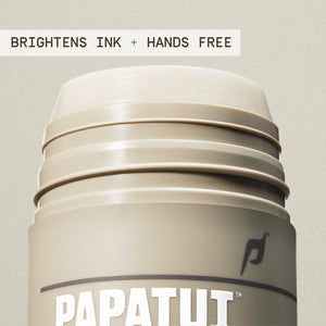 An open container of PAPATUI Enhancing Tattoo Stick highlighting it brightens ink and is hands free.