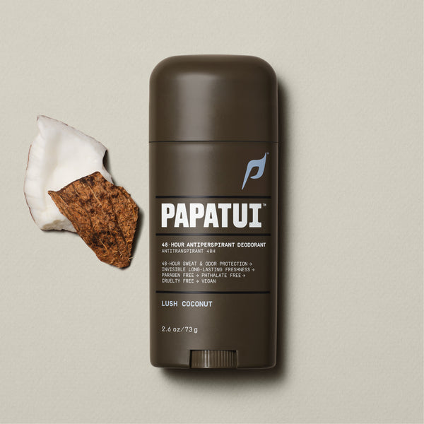 A dark brown stick of PAPATUI 48-Hour Antiperspirant Deodorant in Lush Coconut scent, positioned on a beige background with small dark twigs to the side. The product features orange and white text on the label, promising 48-hour sweat and odor protection, invisibility on clothes, and long-lasting freshness. The deodorant's size is indicated as 2.6 ounces or 73 grams.