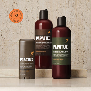 A PAPATUI men's personal care bundle displayed on a marble surface. The set includes a 48-Hour Antiperspirant Deodorant in Sandalwood Suede scent in a brown stick form, a Nourishing Shampoo-Conditioner, and a Refreshing Body Wash, both in Sandalwood Suede scent, housed in translucent brown bottles with black caps and green labels detailing their benefits.