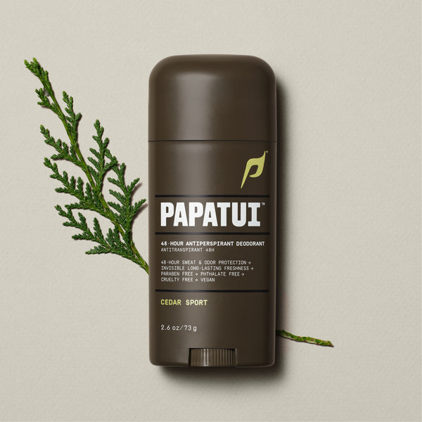 A dark brown stick of PAPATUI 48-Hour Antiperspirant Deodorant in Cedar Sport scent, positioned on a beige background with small dark twigs to the side. The product features orange and white text on the label, promising 48-hour sweat and odor protection, invisibility on clothes, and long-lasting freshness. The deodorant's size is indicated as 2.6 ounces or 73 grams.